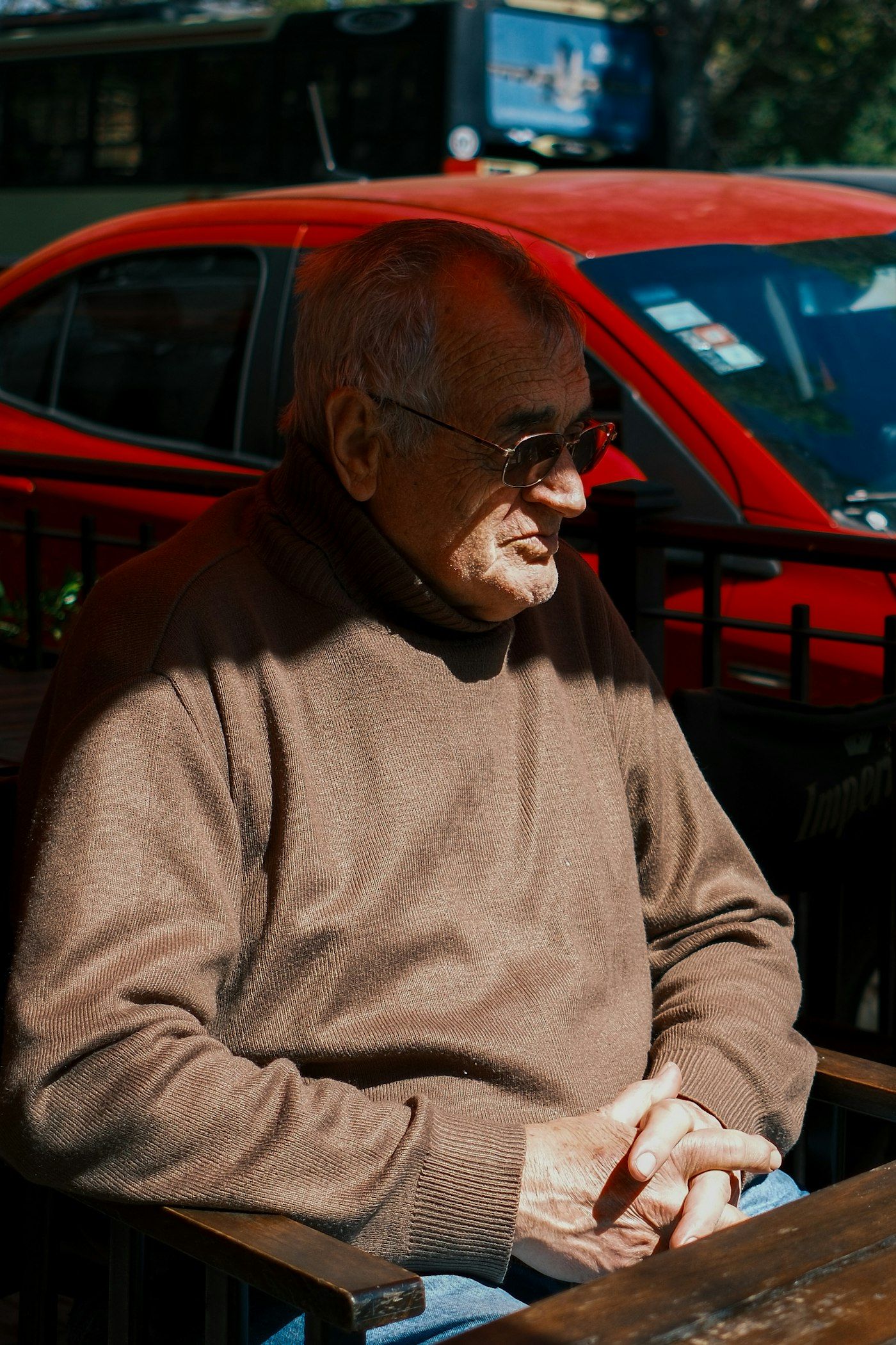 Older man in sunglasses and a beige sweater sitting outdoors on a sunny day