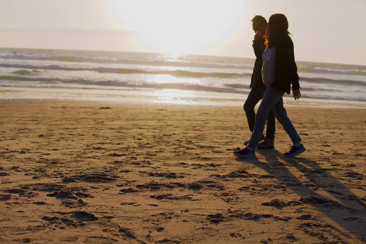 Two women jogging together on a sandy beach at golden hour with ocean waves behind them