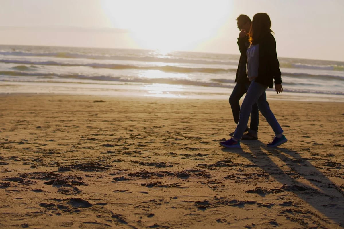 Two women jogging side by side on a sandy beach at golden hour, ocean waves behind them